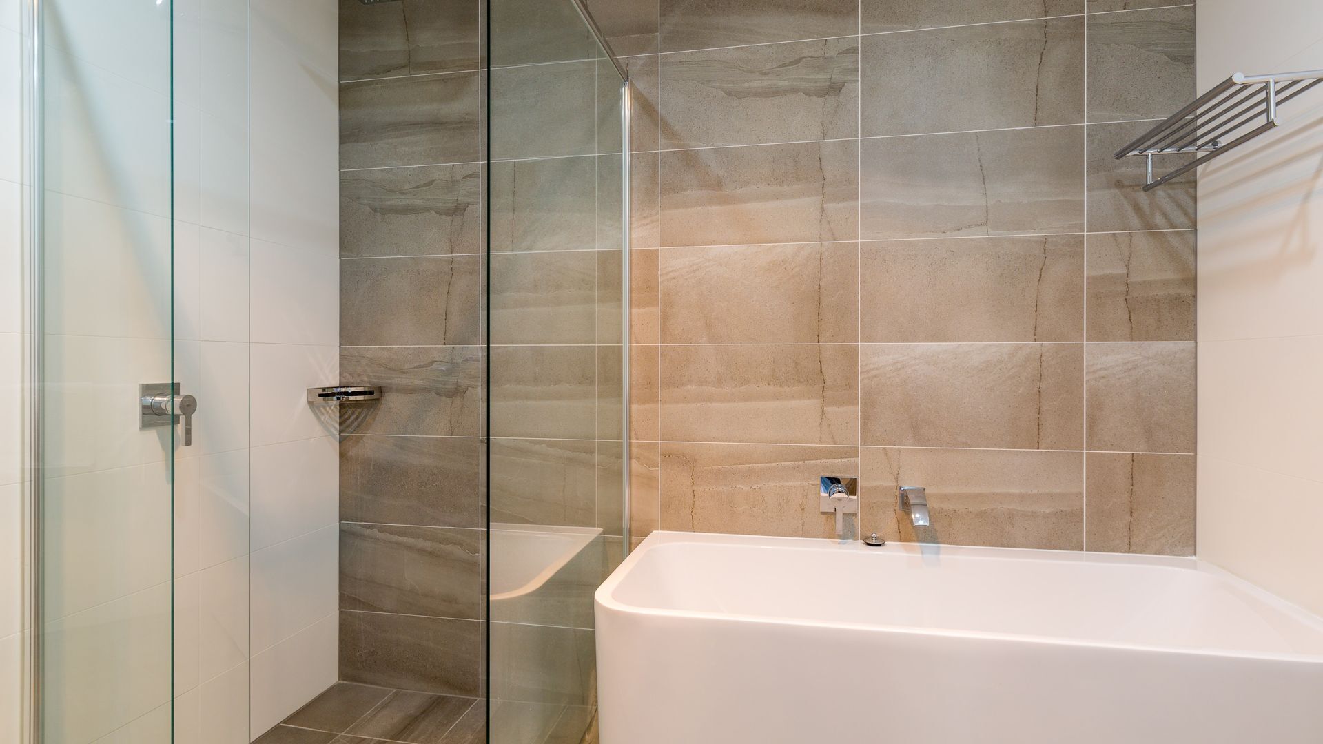 A modern bathroom with a glass shower enclosure, a white bathtub, and a wall-mounted towel rack.