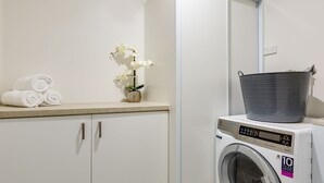 A laundry area with a washing machine, a towel rack with rolled towels, and a potted orchid.