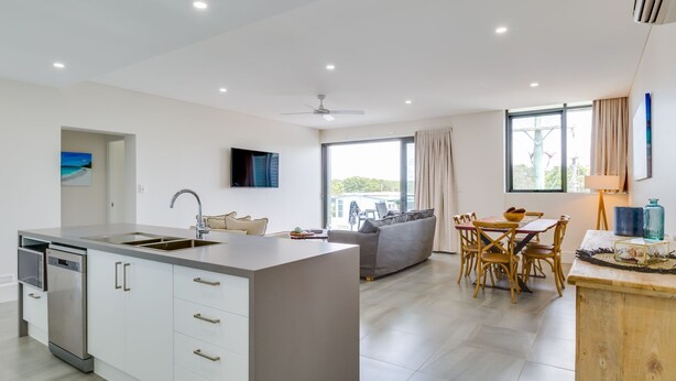 A modern kitchen with a central island, a dining area with a wooden table, and a sofa.