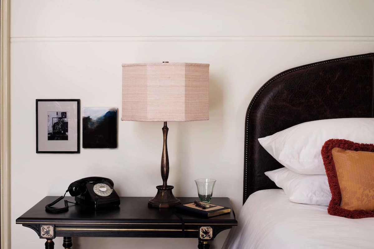 Quarto de hotel bem organizado com uma cama, mesa de cabeceira com abajur, telefone e quadros nas paredes.