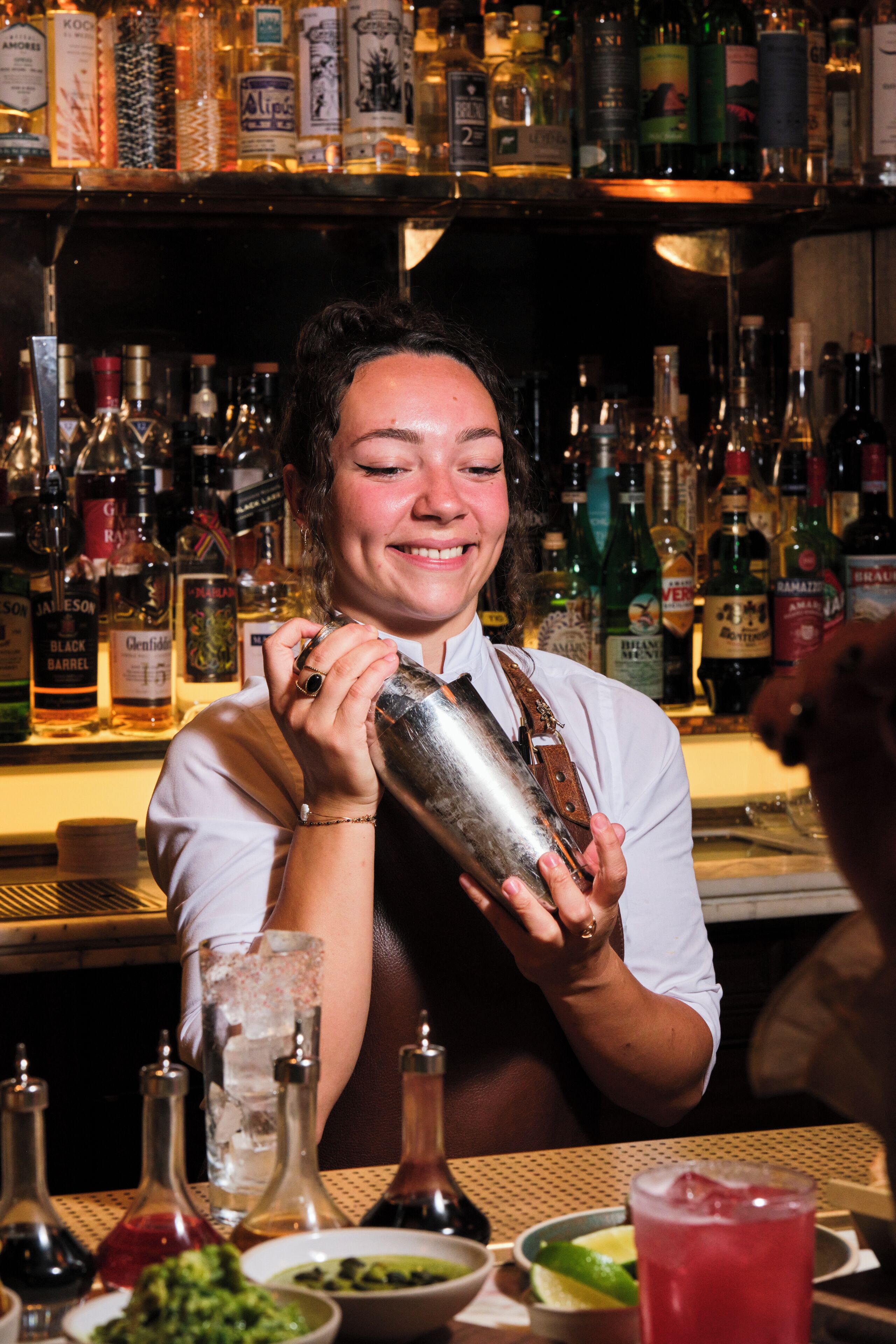 Un barman prépare un cocktail derrière un comptoir, avec différentes bouteilles et différents verres à portée de main.