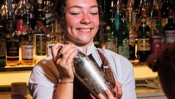 Un barman prépare un cocktail derrière un comptoir, avec différentes bouteilles et différents verres à portée de main.