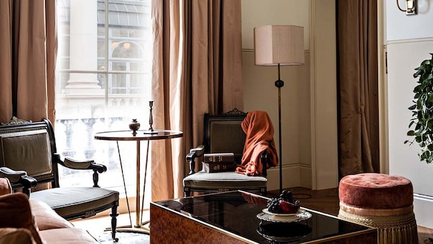 A room with a classic chair, a small round table, a sofa, a coffee table, and a lamp.