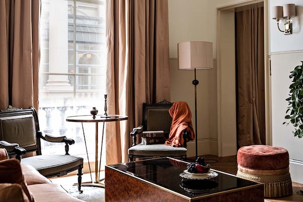 Una habitación con una silla clásica, una mesita redonda pequeña, un sofá, una mesa de centro y una lámpara.