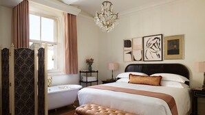 A bedroom with a large bed, a vanity, a bathtub, and a chandelier.
