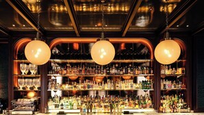 A bar area with a marble countertop, multiple stools, and a variety of bottles and glasses on shelves. - NoMad London (London)