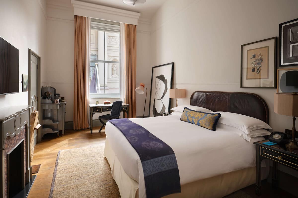 Quarto de hotel com uma cama grande, uma escrivaninha com cadeira, televisão e obras de arte emolduradas nas paredes.