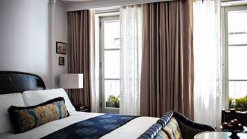 Habitación de hotel con una cama grande, un sofá, una mesa redonda y una ventana con cortinas.