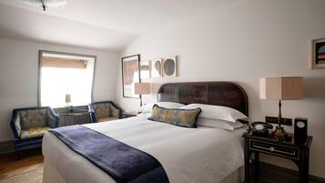 A hotel room with a large bed, a sitting area with a chair, a desk with a lamp, and a wall-mounted telephone.