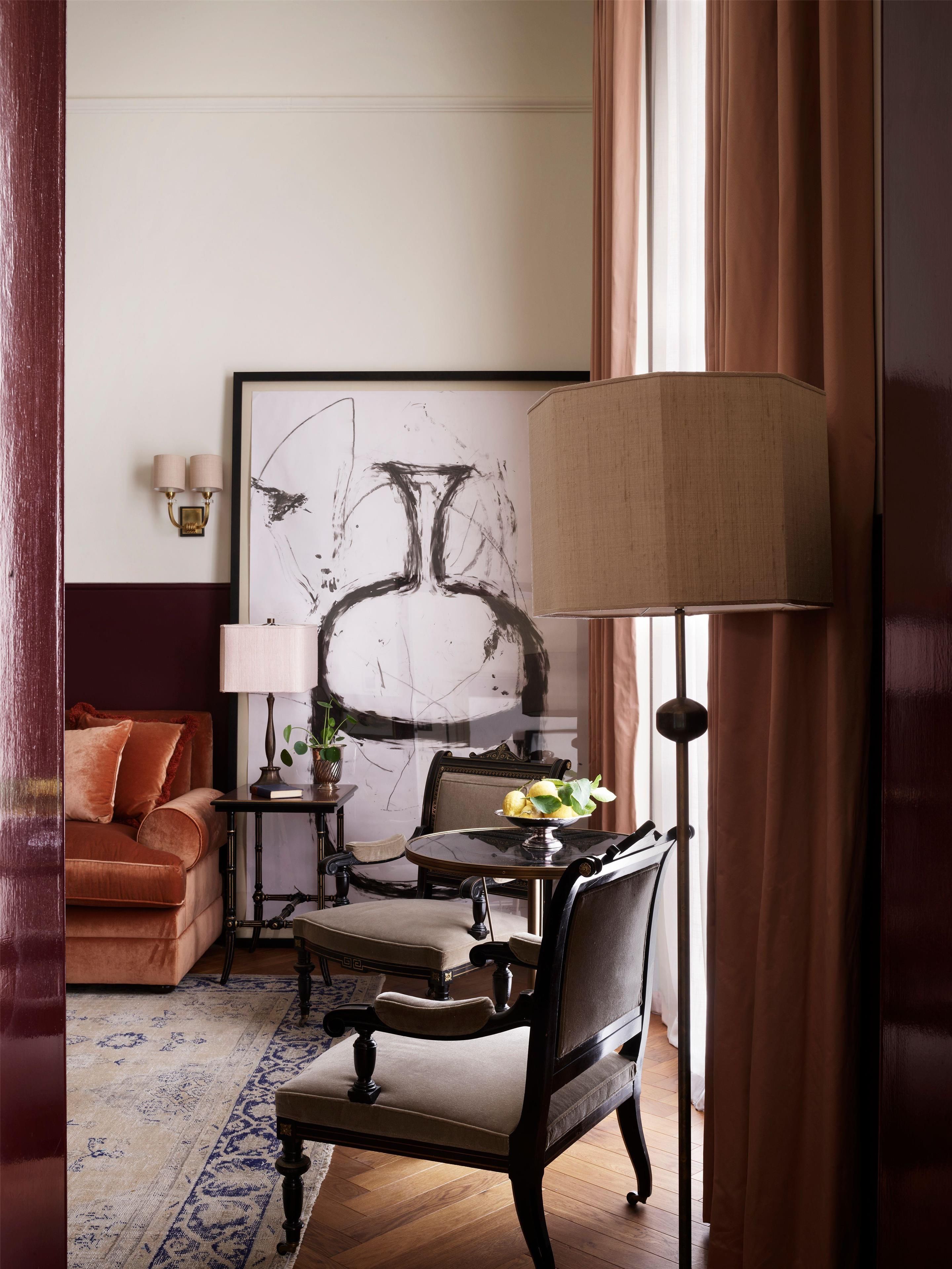 Una habitación con un sofá, una mesa con lámpara, una silla y un cuadro abstracto grande en la pared.