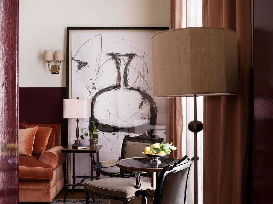 Una habitación con un sofá, una mesa con lámpara, una silla y un cuadro abstracto grande en la pared.