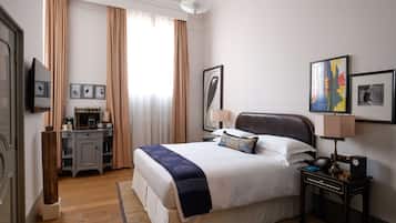 Habitación de hotel con una cama grande, un escritorio con lámpara y un televisor en la pared.