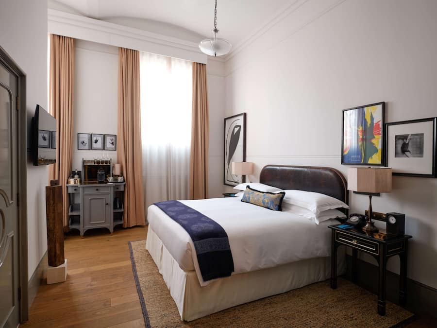 Habitación de hotel con una cama grande, un escritorio con lámpara y un televisor en la pared.