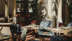 A dining area with wicker chairs, a round table, and a large potted plant.