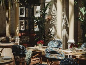 A dining area with wicker chairs, a round table, and a large potted plant. - NoMad London (London)