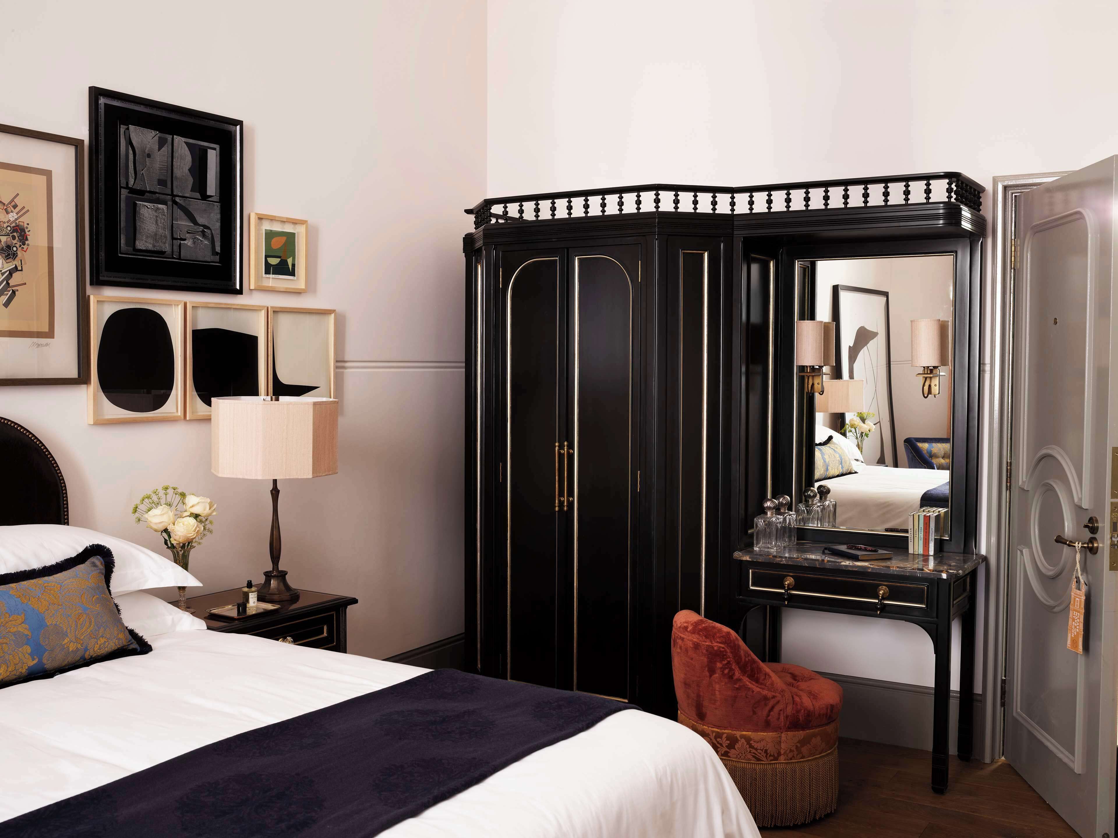 Una camera d'albergo con un letto, una toeletta con specchio, una sedia rossa e un armadio.