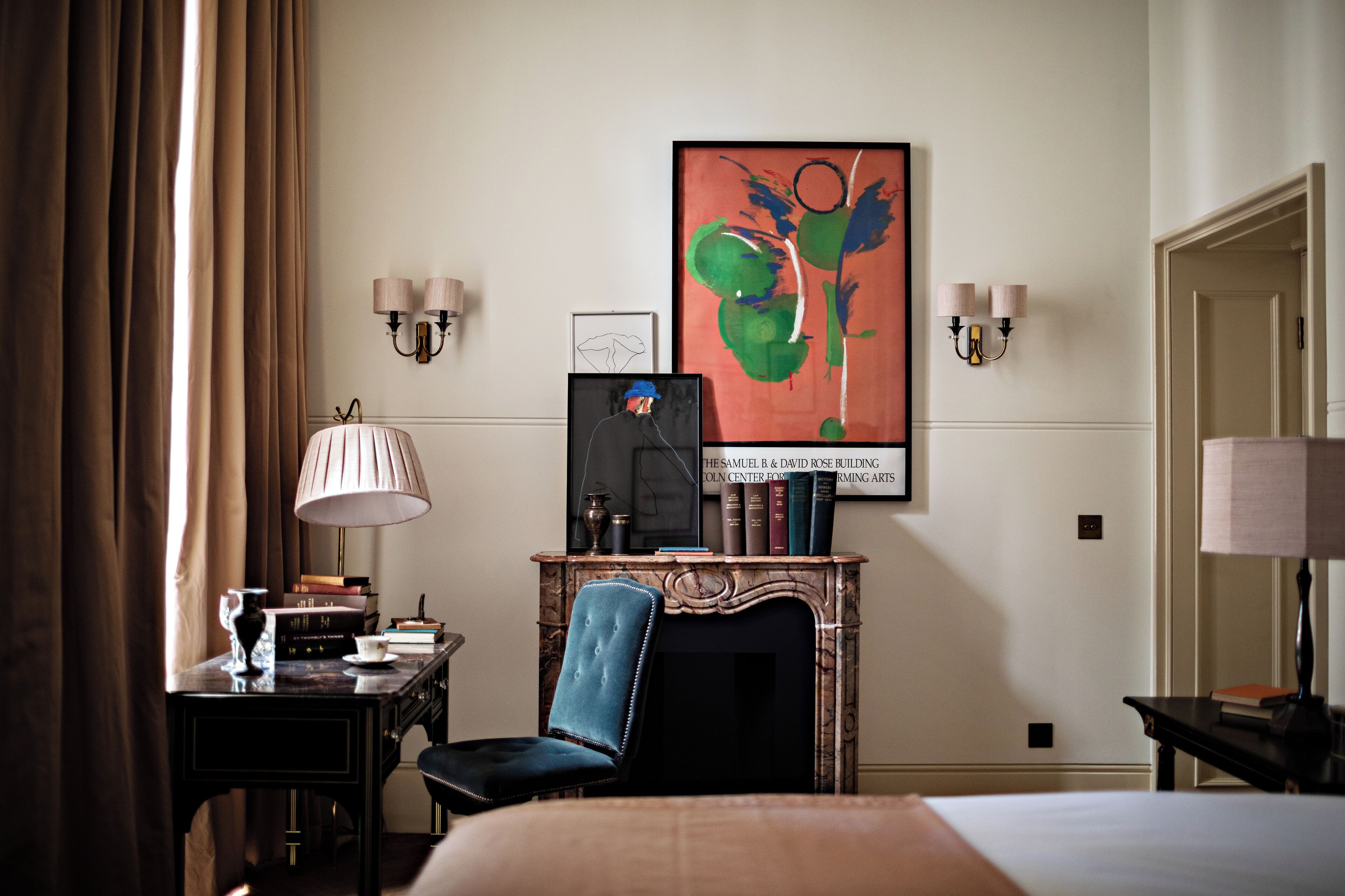 Ein Hotelzimmer mit Bett, Schreibtisch mit Lampe, Sessel und Kamin. An der Wand hängt ein großes, abstraktes Gemälde.