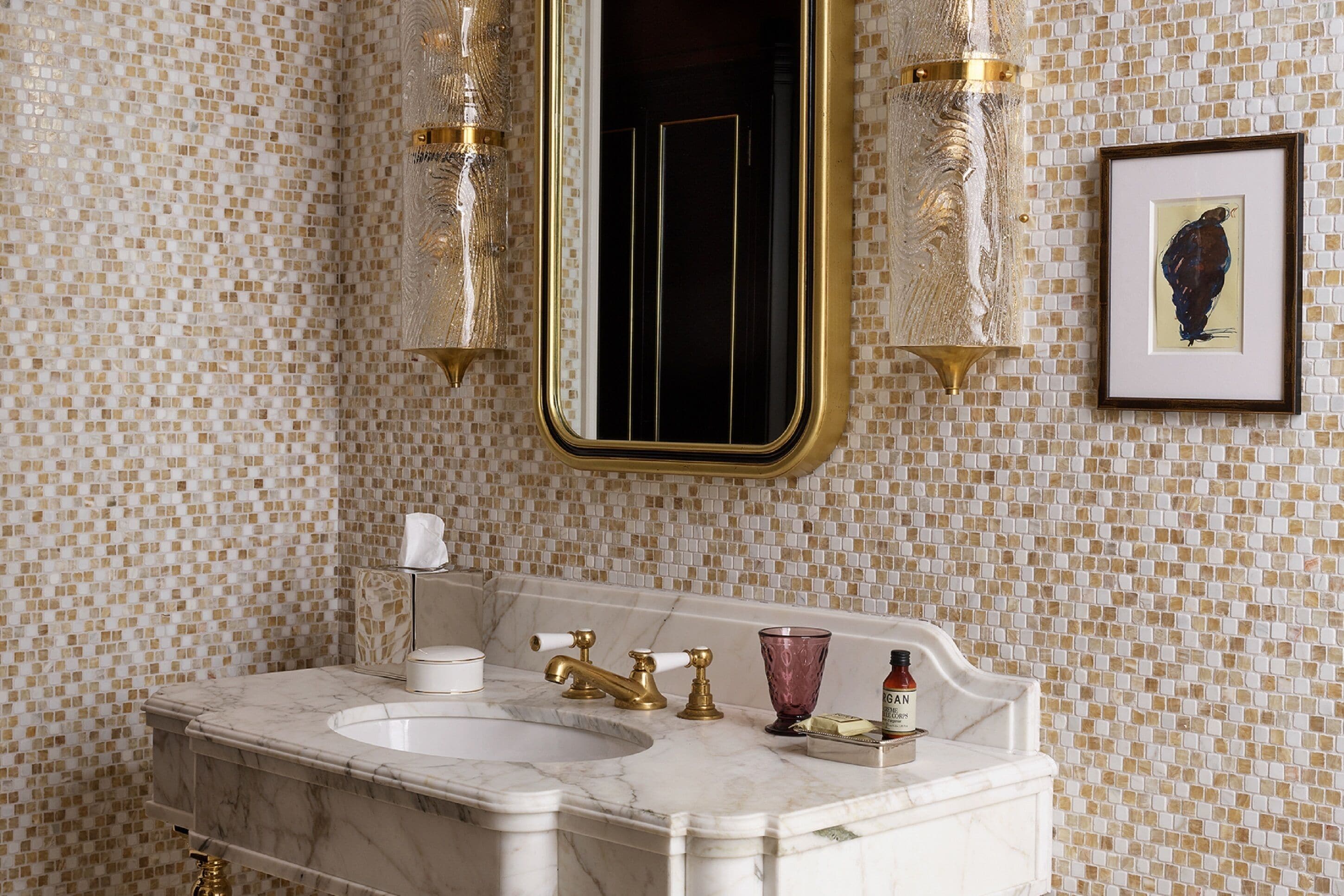 A bathroom with a marble sink, gold faucets, and mosaic tile walls.