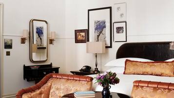 A hotel room with a bed, a sitting area with a chair and a table, a chandelier, and artwork on the wall.