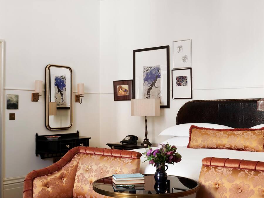 A hotel room with a bed, a sitting area with a chair and a table, a chandelier, and artwork on the wall.