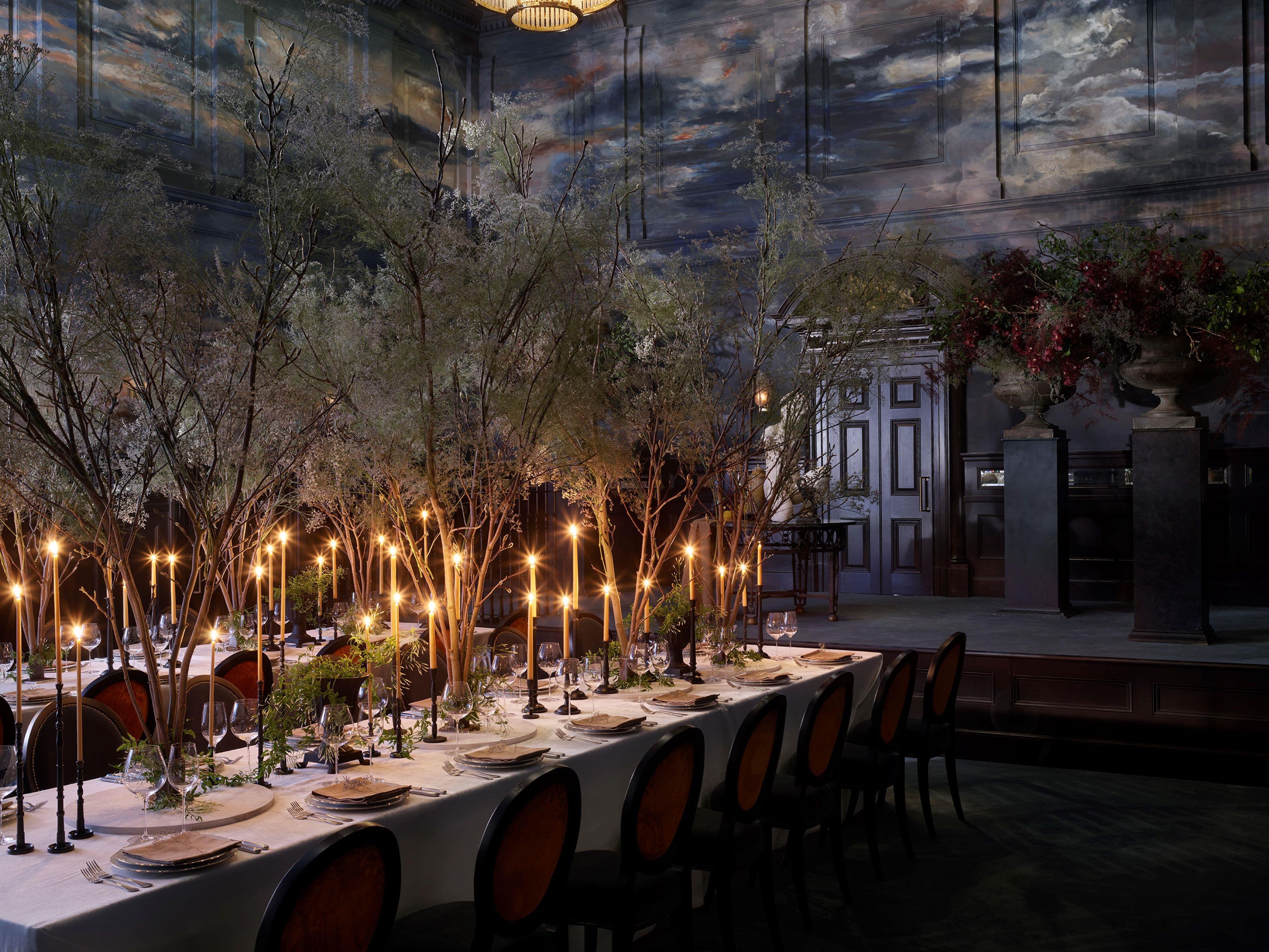 Una larga mesa de comedor dispuesta con velas, sillas y vista a un edificio con un mural.