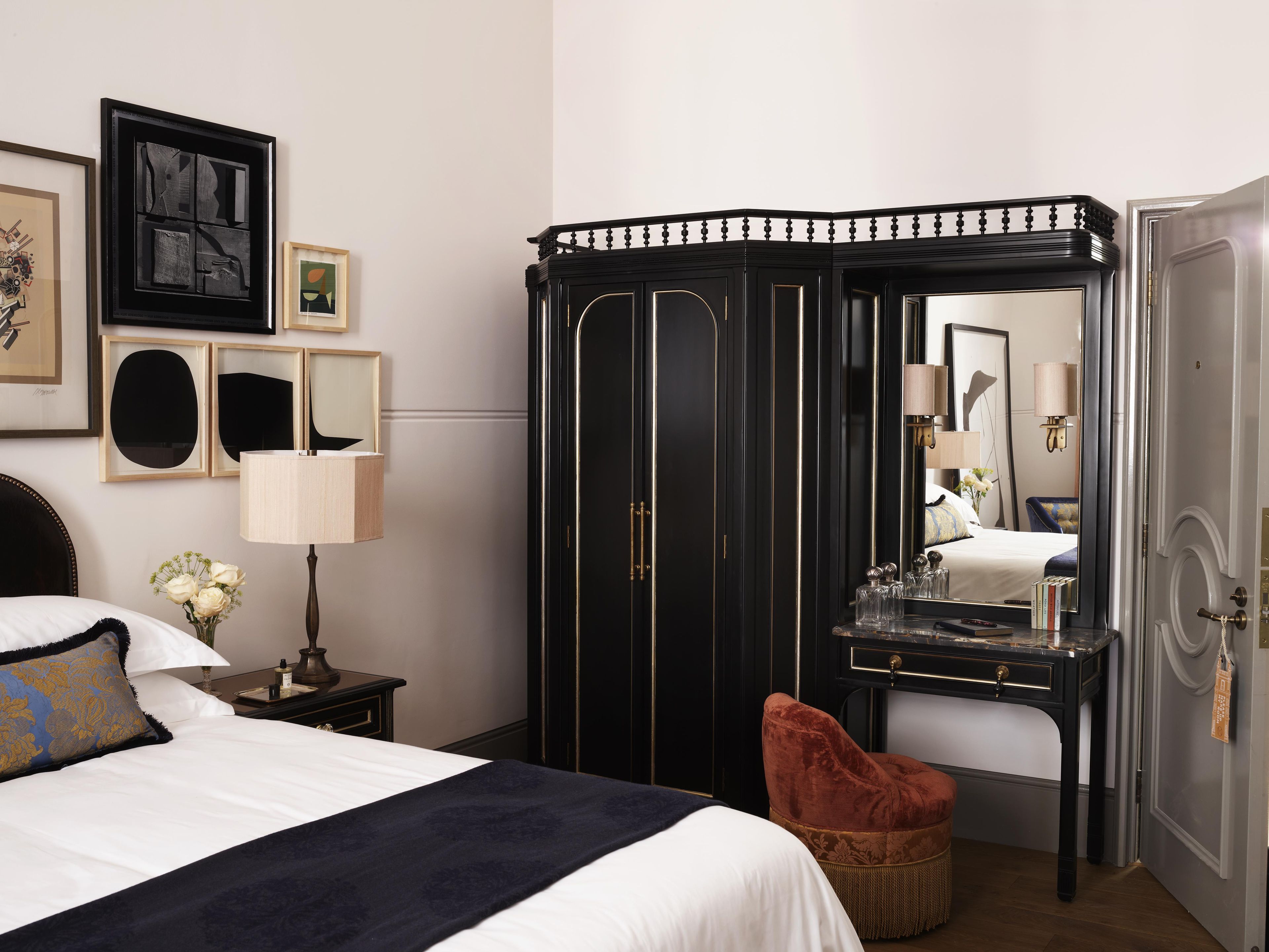 A hotel room with a bed, a vanity with a mirror, a wardrobe, and a red chair.