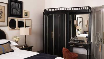 A hotel room with a bed, a vanity with a mirror, a wardrobe, and a red chair.