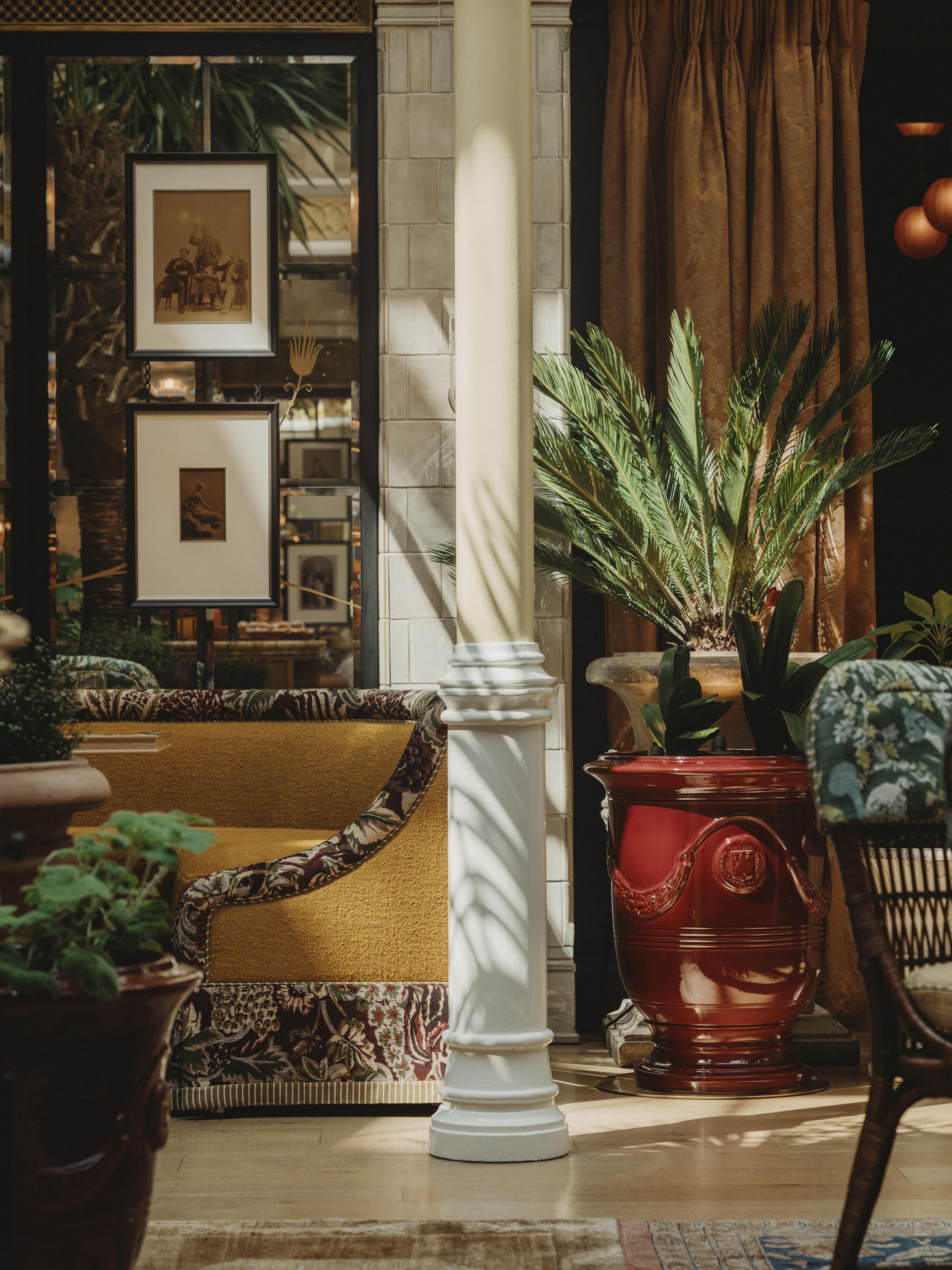 Un salon chaleureux avec un canapé à motifs, un pot de fleurs rouge et une colonne blanche.