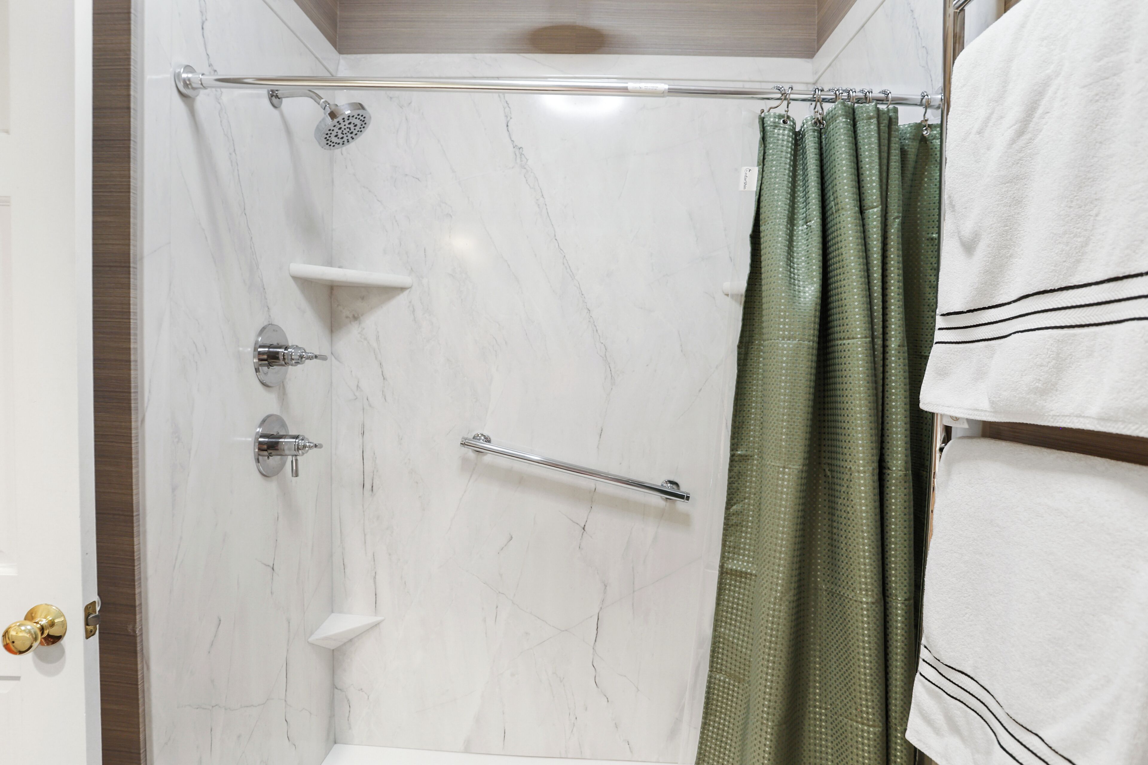 Een badkamer met een douche, een handdoekhouder en een deur met een koperen handvat.