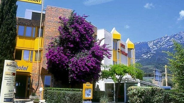 Un hotel con un letrero amarillo, fachada de ladrillo y flores moradas al frente.