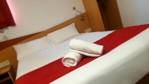 Una habitación de hotel con una cama bien hecha, una colcha roja y blanca, y una toalla blanca doblada sobre la cama.