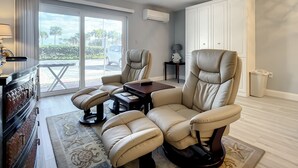 A spacious living room with a large sliding glass door leading to a balcony, a leather sofa set, a small table, and a white wardrobe.