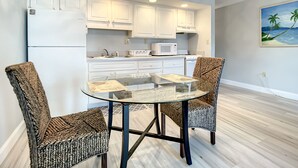 A modern kitchen with white cabinets, a glass dining table, and two patterned chairs.