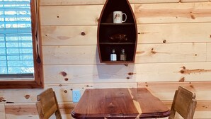 Un intérieur en bois avec une table et deux chaises, une étagère avec une tasse et des bouteilles, et une fenêtre avec des stores.