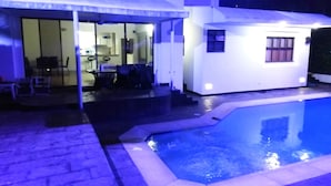 A pool area with a small building and a covered seating area.