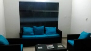 A living room with a black sofa and two armchairs, both with blue cushions.