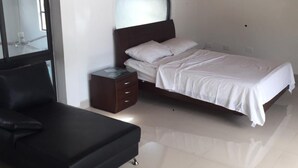 A bedroom with a bed, a nightstand, a chair, and a large mirror.