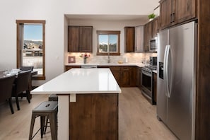 A modern kitchen with wooden cabinets, a stainless steel refrigerator, and a large island. - 219 Elk Ranch Private Hot Tub (Fraser)