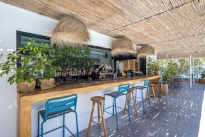 A bar area with a wooden counter, blue chairs, and hanging thatch lamps. - Kamari Beach (Santorini)