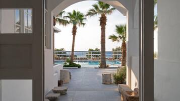 Zona de piscina exterior con palmeras, vista despejada al mar y un sendero de piedra que conduce a zonas de estar.