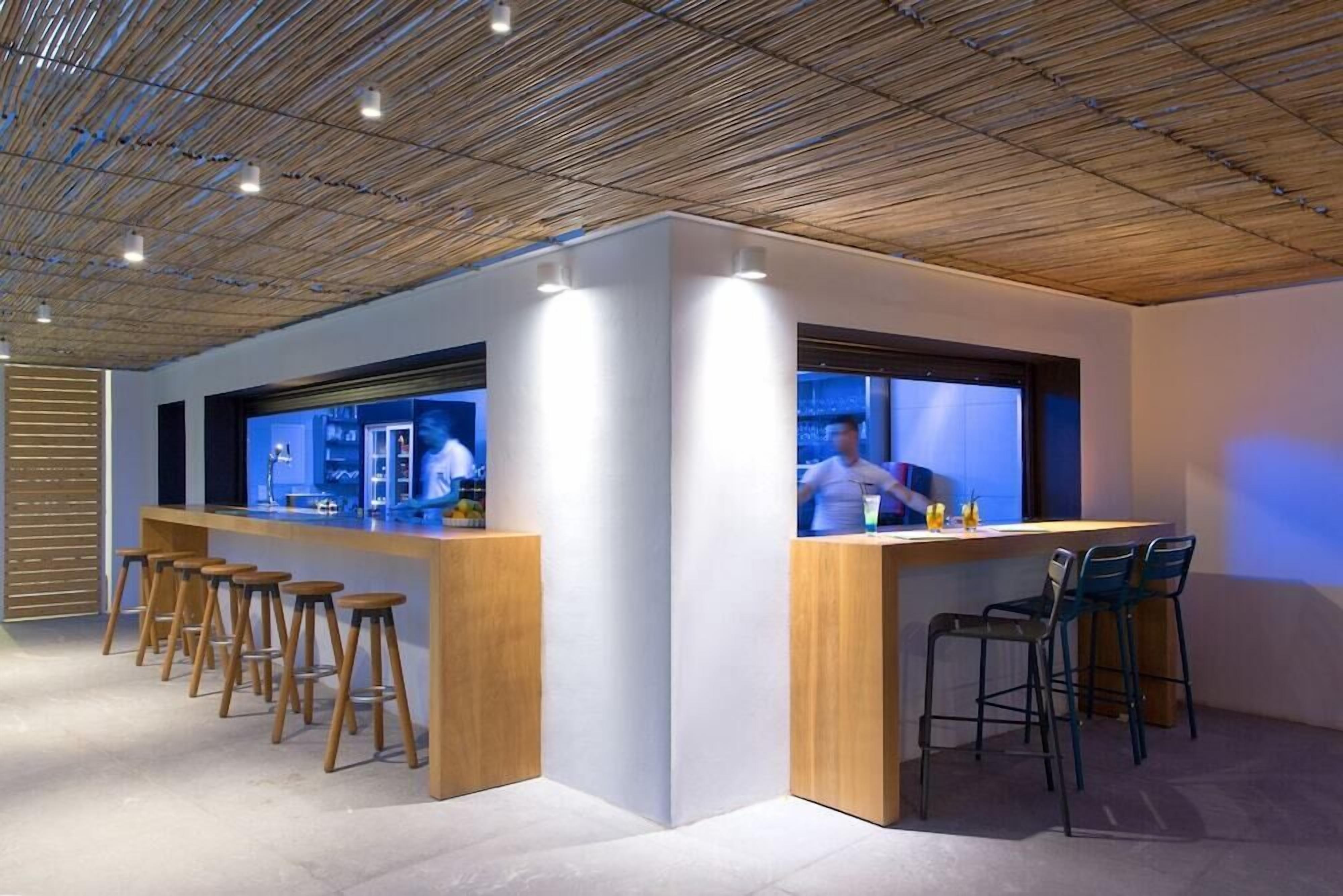 Un espace bar moderne avec des tabourets en bois et un comptoir, doté d’un design de plafond original et d’un éclairage d’ambiance.