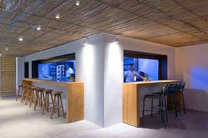 Zona de bar moderna con taburetes de madera y una barra, destacando un diseño de techo único e iluminación ambiental.