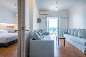 Habitación de hotel moderna con cama, sofá, una mesita y televisor. Tiene un balcón con vistas.