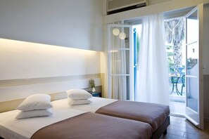 A hotel room with two beds, a nightstand, and a view of the outdoor area. - Kamari Beach (Santorini)