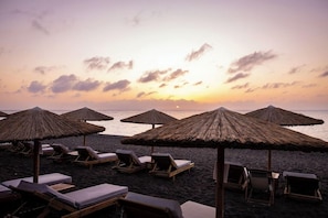 A beach with lounge chairs and thatched umbrellas, suggesting a resort setting. - Kamari Beach (Santorini)