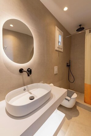 Un baño moderno con un lavamanos ovalado grande, un espejo, una ducha y un inodoro.