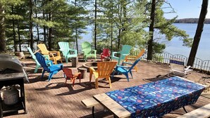 Un espacio al aire libre con sillas Adirondack de colores, una mesa de madera con mantel floral y una parrilla.