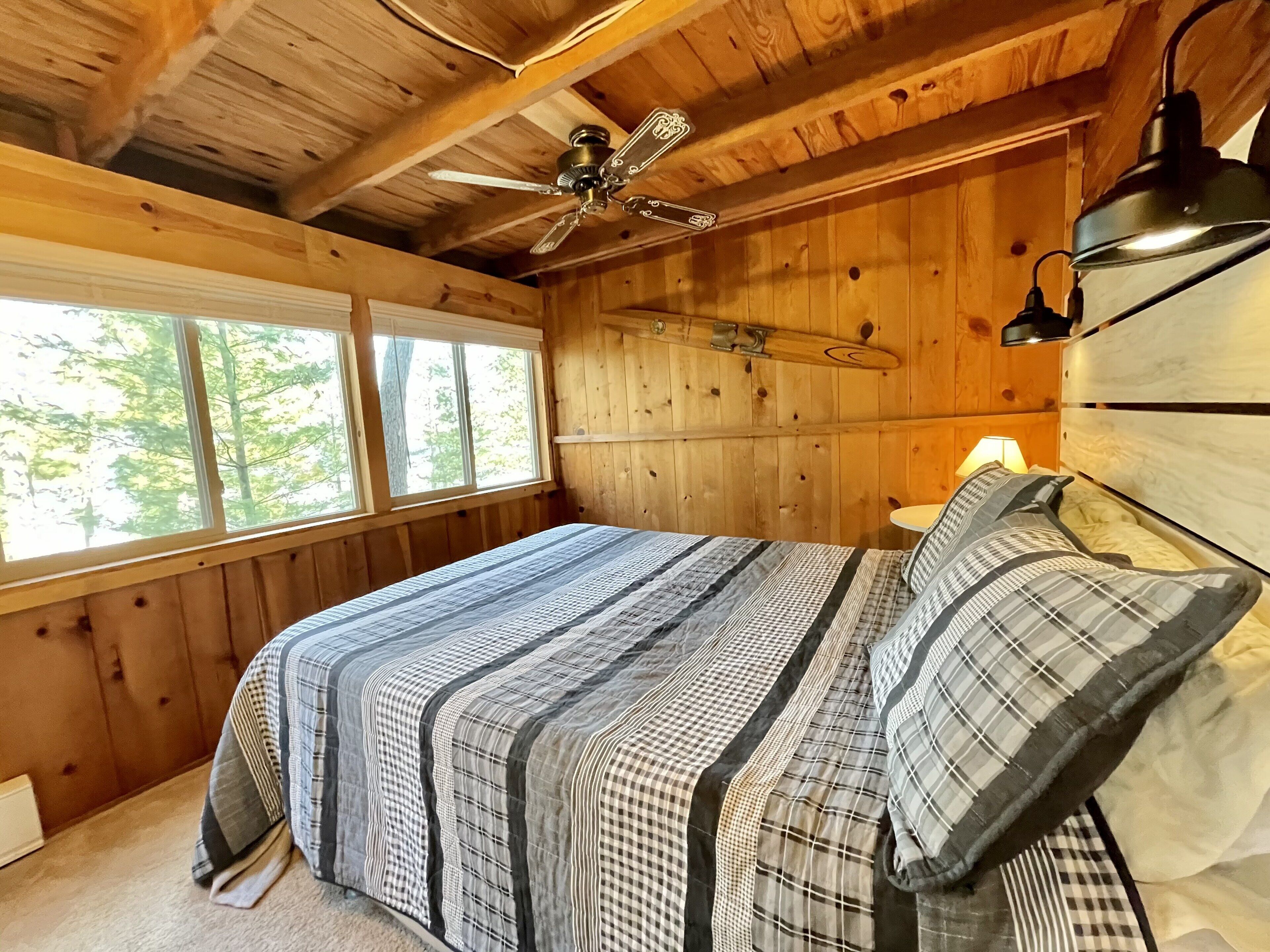 A wooden cabin bedroom with a bed, a ceiling fan, and a window.