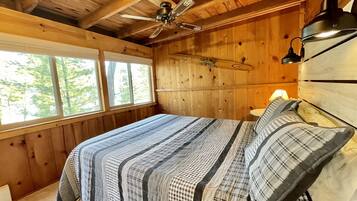 A wooden cabin bedroom with a bed, a ceiling fan, and a window.