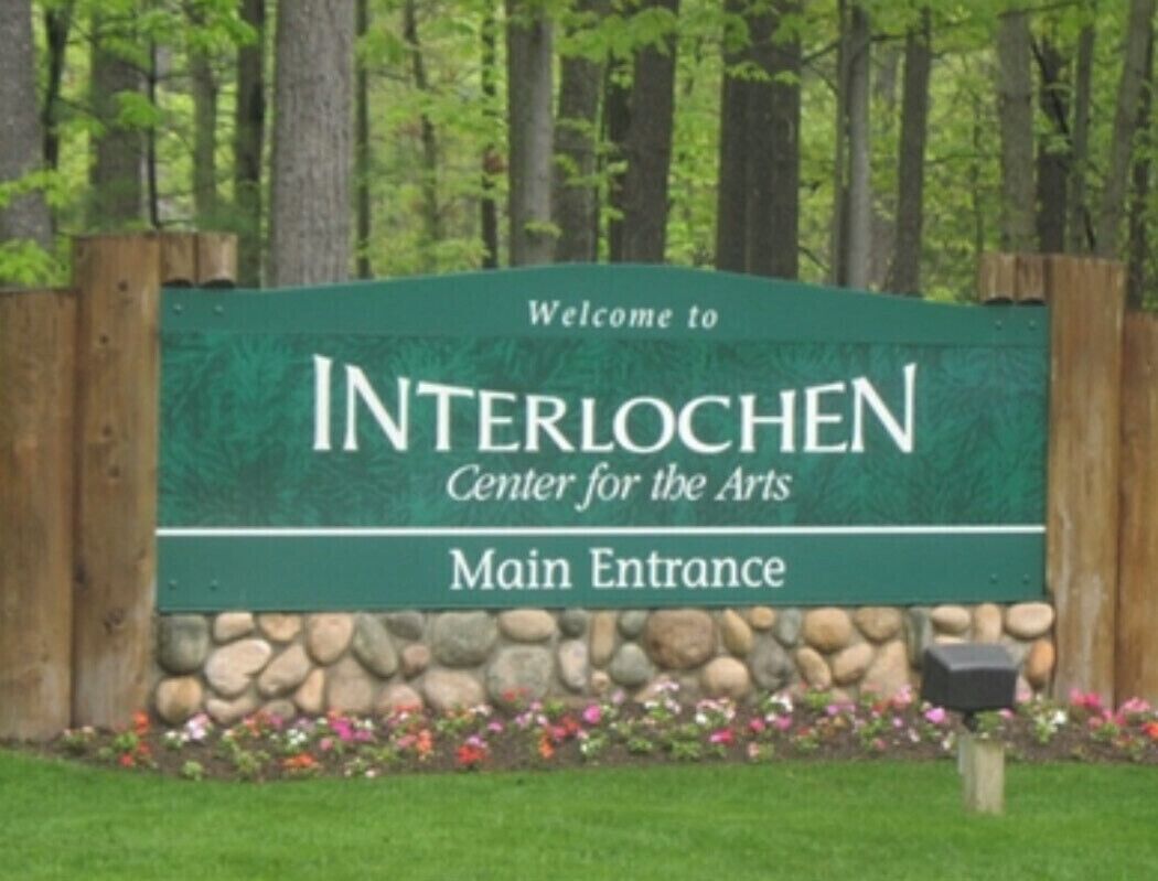 A sign for the Interlochen Center for the Arts with a stone wall and flower bed in front.